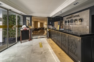 Un moderno vestíbulo de hotel con una recepción, un panel de vidrio y una planta decorativa.