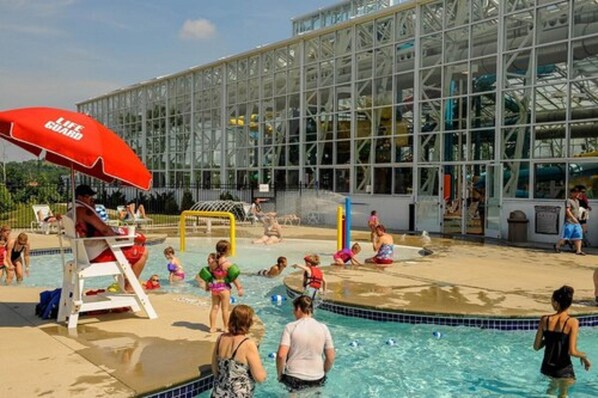 A swimming pool area with a glass building in the background, a lifeguard stand, and a red umbrella.