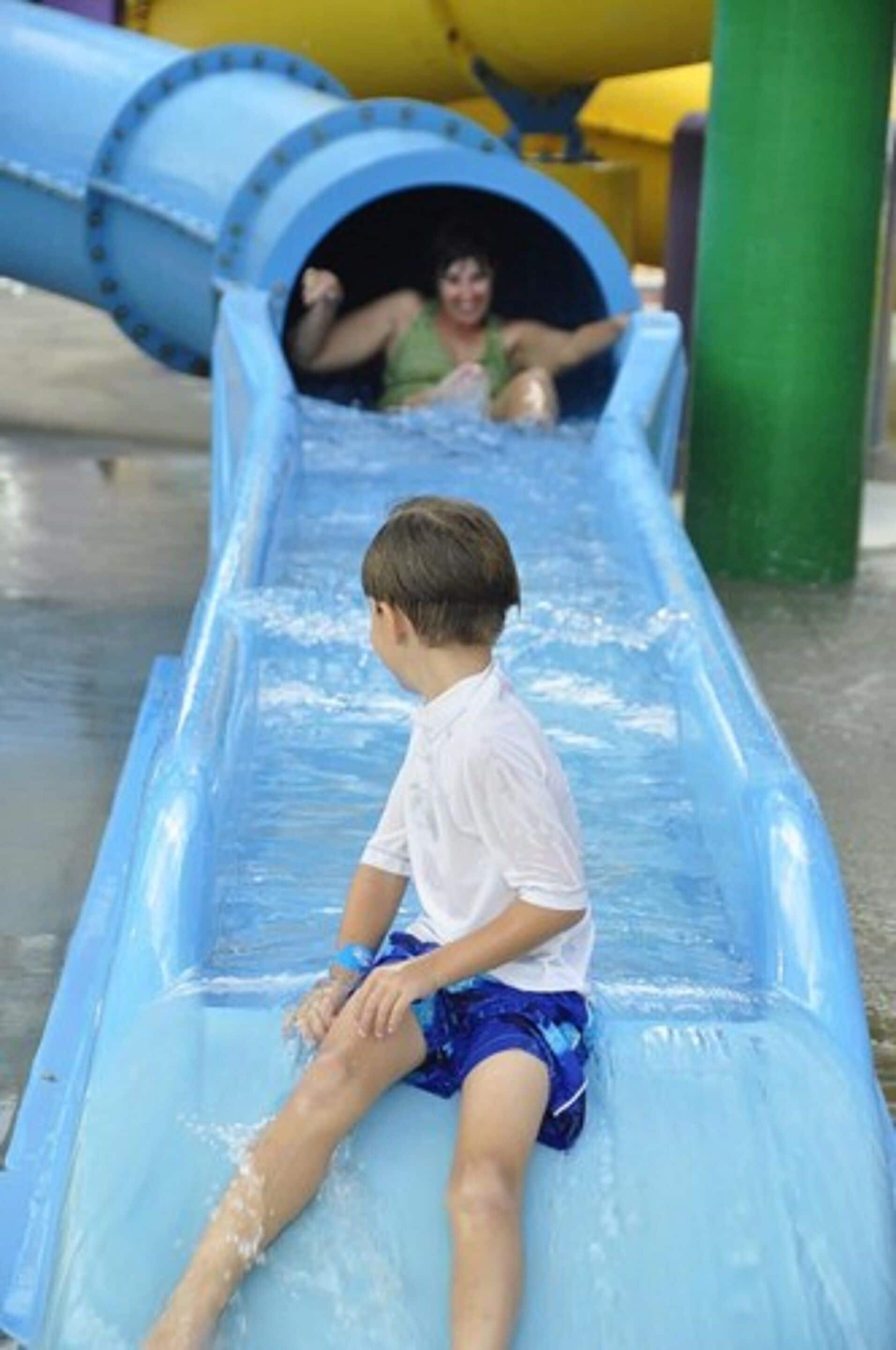A child sliding down a blue water slide at a water park.