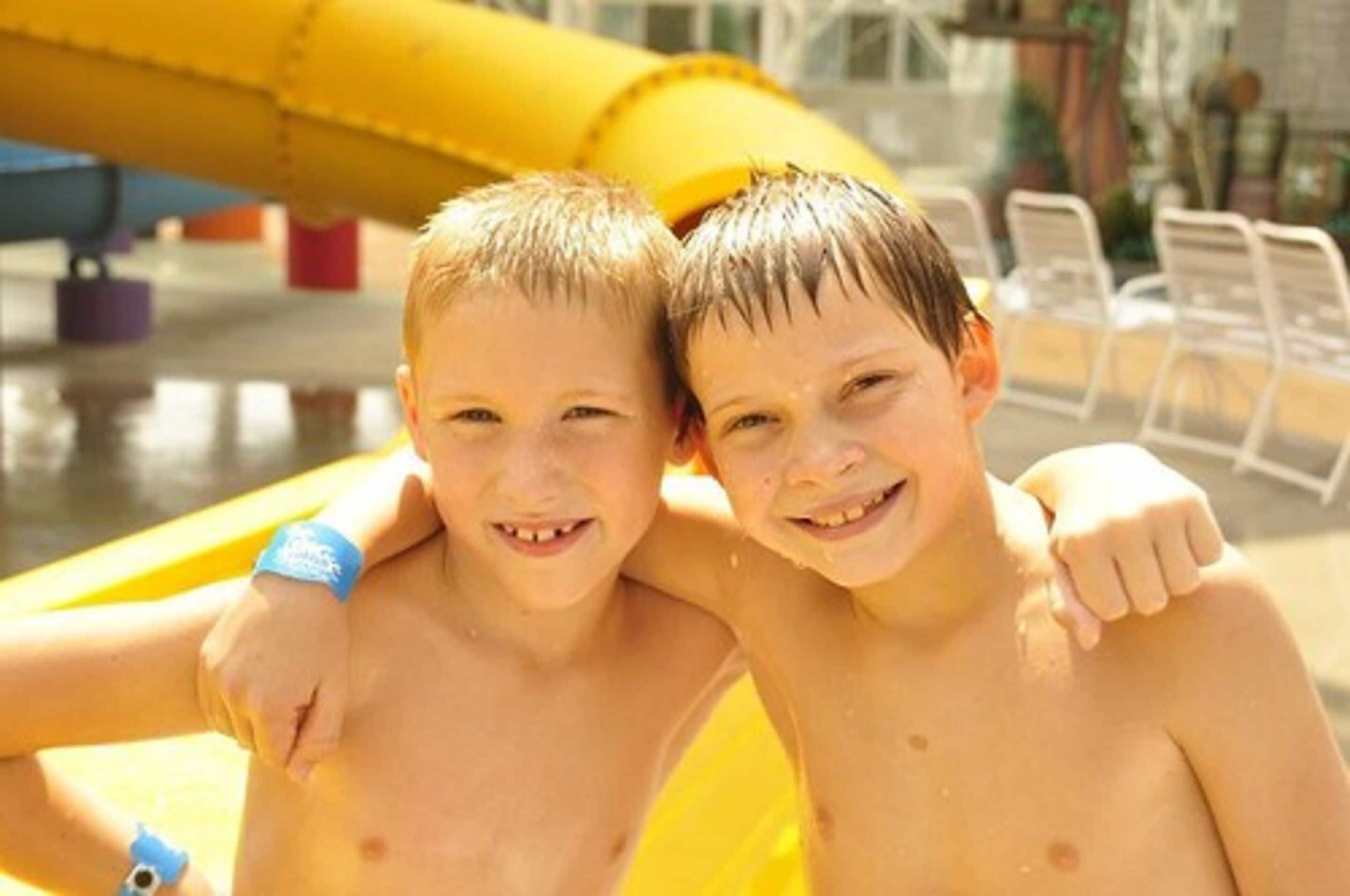 Two children in a pool area with a yellow slide in the background.