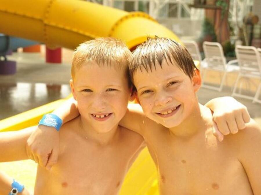 Two children in a pool area with a yellow slide in the background.