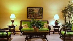 Een hal met een groene bank, twee bijzettafels met lampen, een schilderij aan de muur en planten in potten.