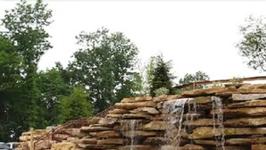 Een waterval met een bankje in een aangelegde tuin.