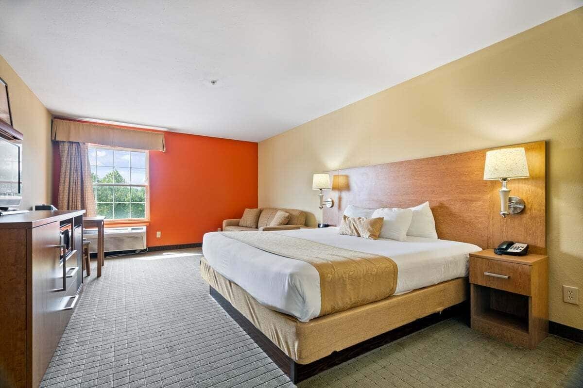 Une chambre d’hôtel avec un grand lit, des lampes de chevet, un bureau et une vue sur la verdure.