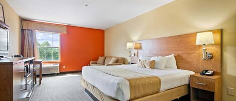 A hotel room with a large bed, bedside lamps, a desk, and a view of greenery outside.