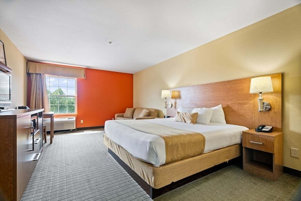 A hotel room with a large bed, bedside lamps, a desk, and a view of greenery outside.