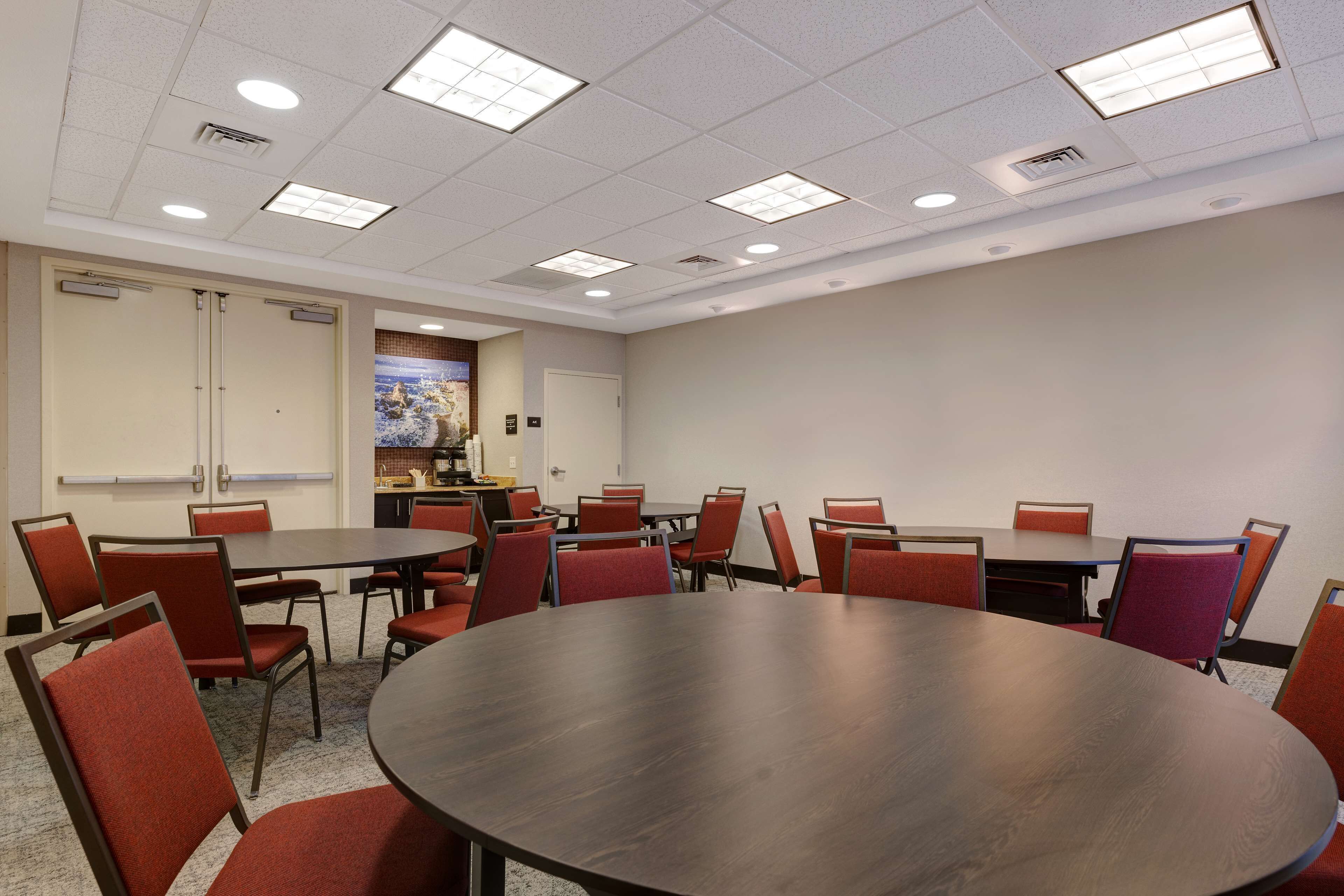 A conference room with a large round table, multiple chairs, and a kitchenette area.