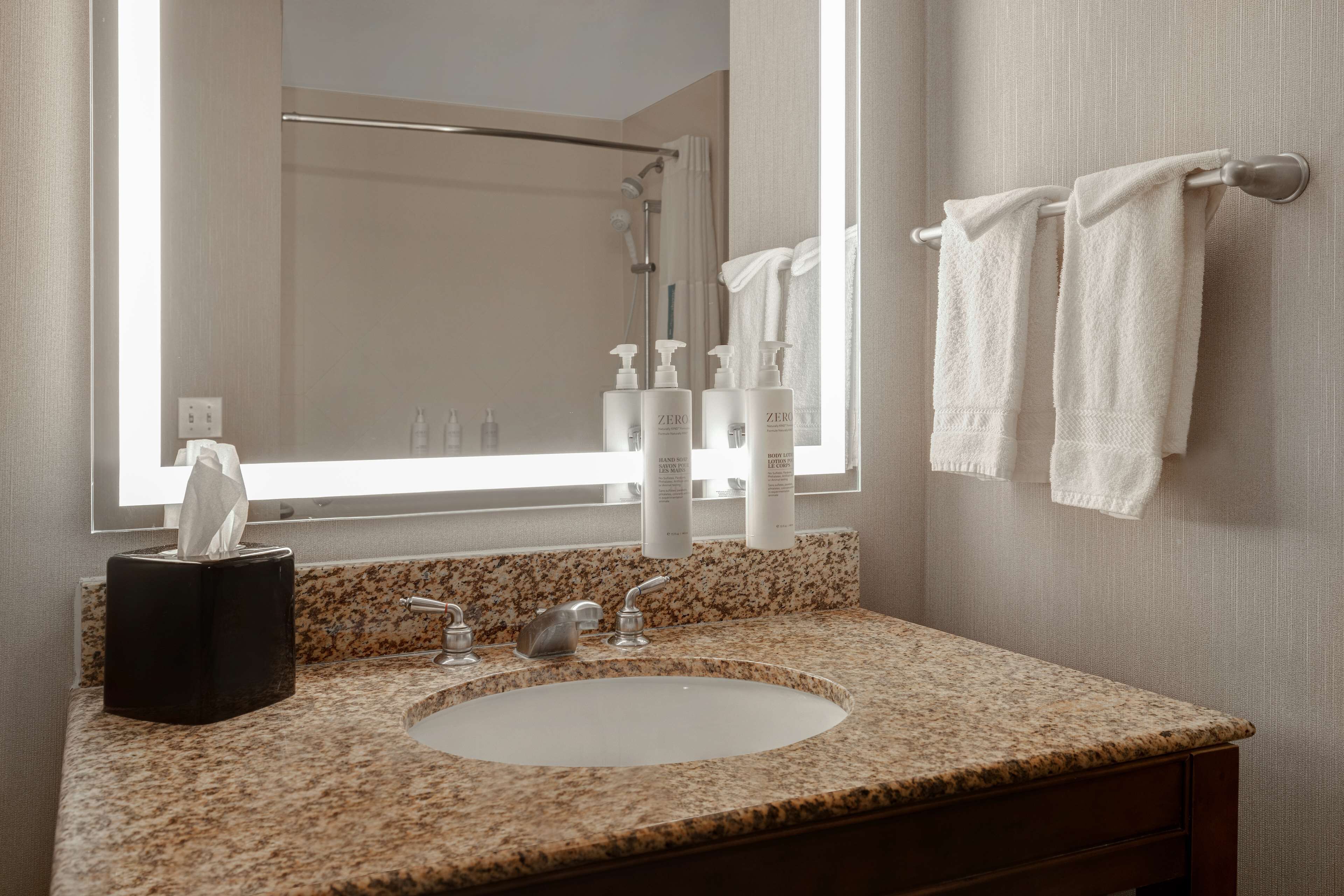A bathroom with a granite countertop, a sink, a mirror, a towel rack, and toiletries.