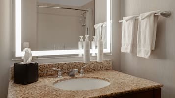 A bathroom with a granite countertop, a sink, a mirror, a towel rack, and toiletries.