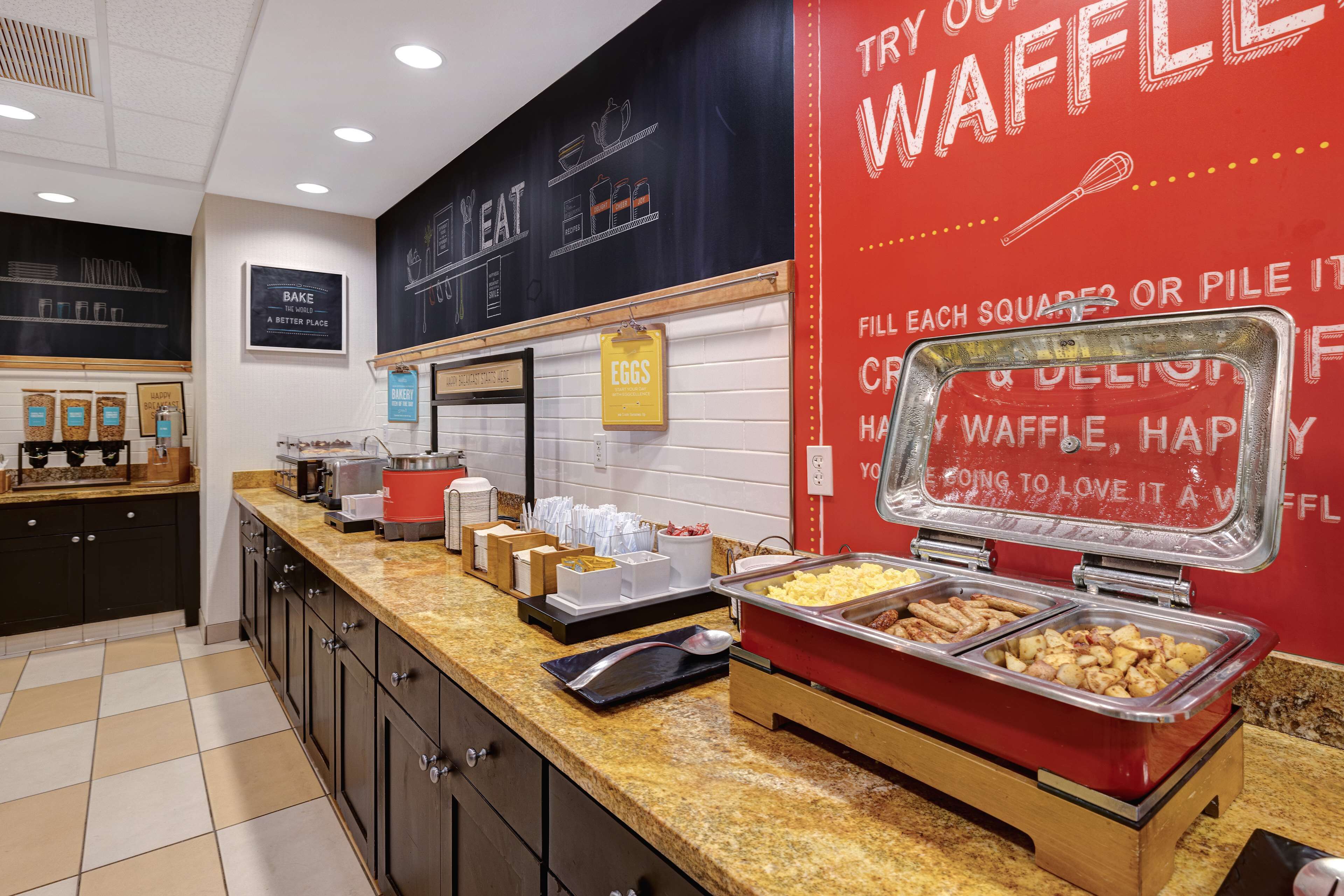 Un espace buffet avec différents stands de nourriture, dont un stand dédié aux gaufres, et un menu écrit à la craie sur le mur.