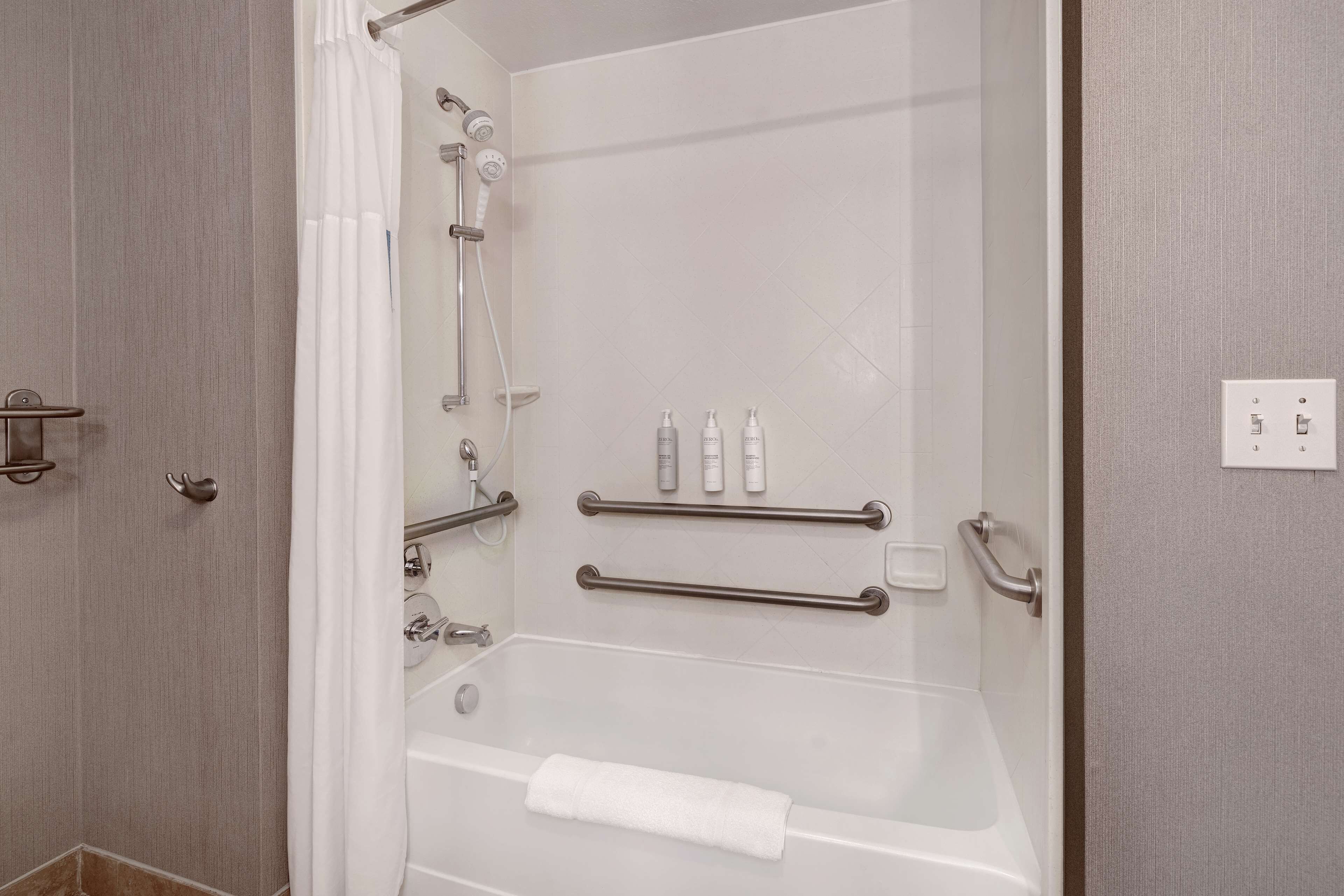 Un baño moderno con ducha acristalada, barras de apoyo y una toalla blanca en el suelo.