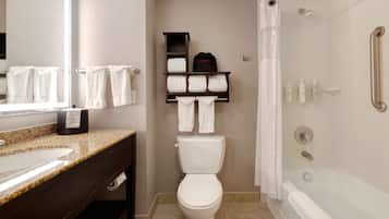 Un baño con lavamanos, inodoro y bañera. Hay toallas colgadas en un perchero y una cortina de ducha.