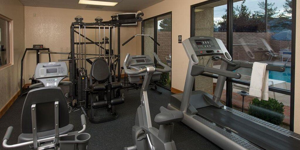 A gym with various exercise equipment, including treadmills and weight machines, and a view of a pool through large windows.