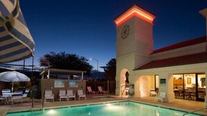 Una piscina con sillas de descanso y una torre con reloj.