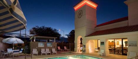 A swimming pool with lounge chairs and a tower with a clock.