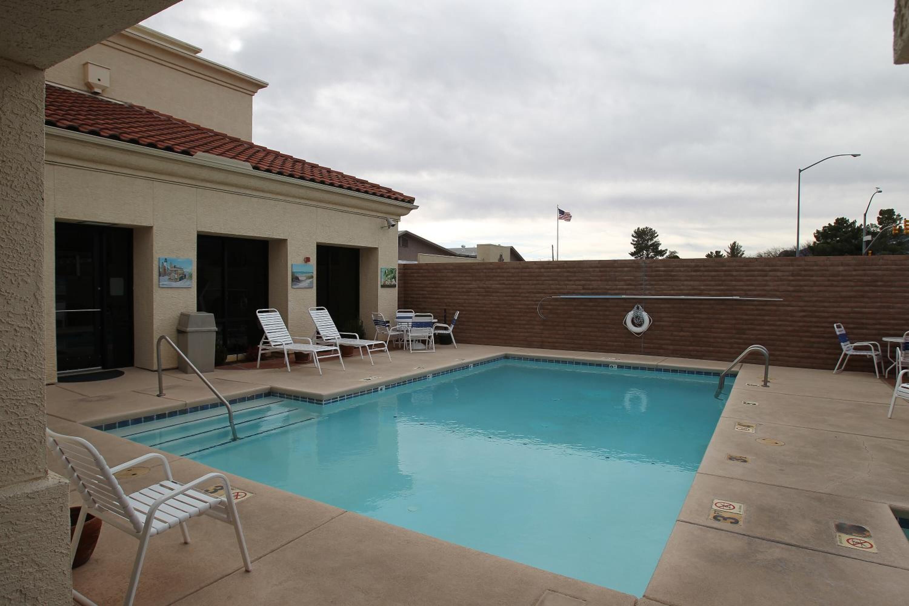 A swimming pool with lounge chairs and a covered area with a brick wall.