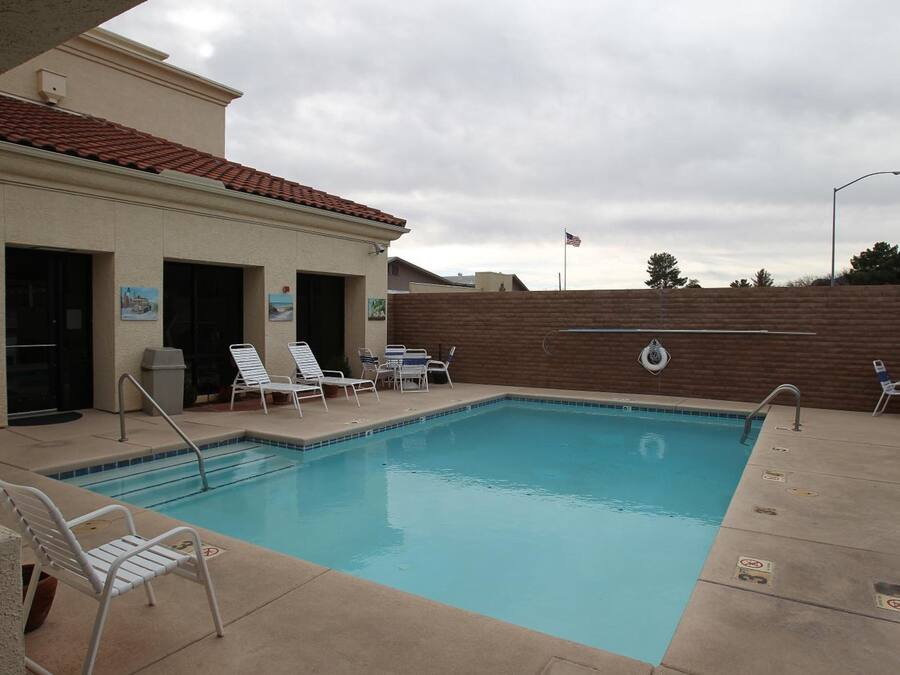 A swimming pool with lounge chairs and a covered area with a brick wall.