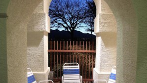 Un espacio de patio al aire libre con un arco de piedra, sillas de metal blanco y una mesa de metal.