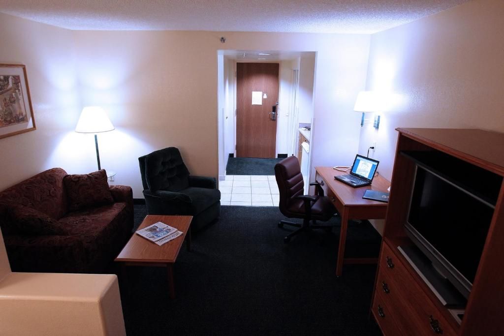 A hotel room with a sofa, a desk with a laptop, a television, and a lamp.