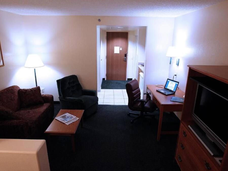 A hotel room with a sofa, a desk with a laptop, a television, and a lamp.
