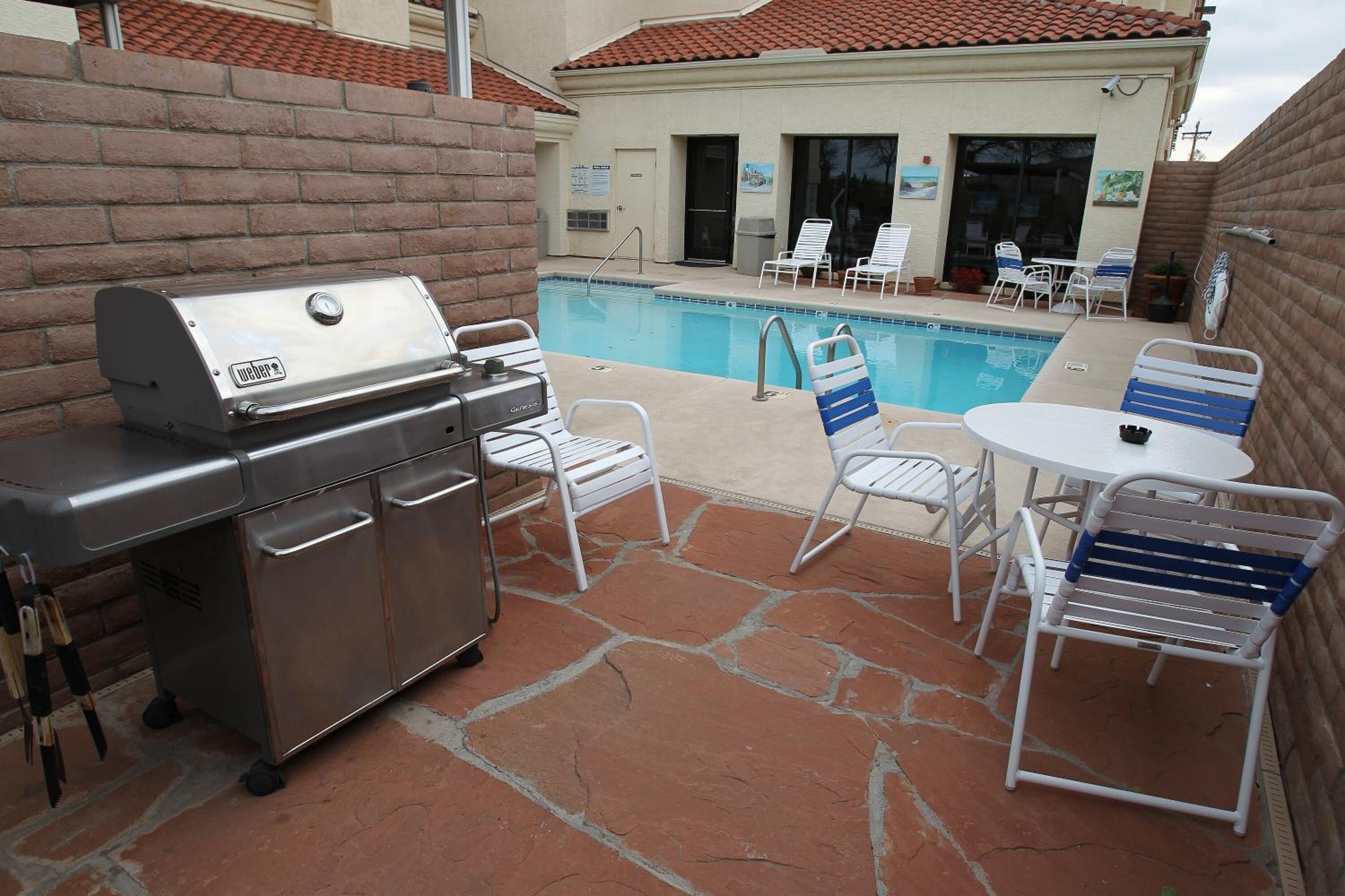 An outdoor patio with a grill, poolside chairs, and a table.