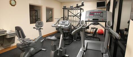 Un gimnasio con equipamiento de ejercicio que incluye cintas de correr, bicicletas estáticas y máquinas de pesas.