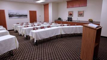 A conference room with multiple tables, a podium, and a kitchen area with a counter and appliances.