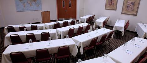 A conference room with multiple tables and chairs, equipped with water glasses and notepads.