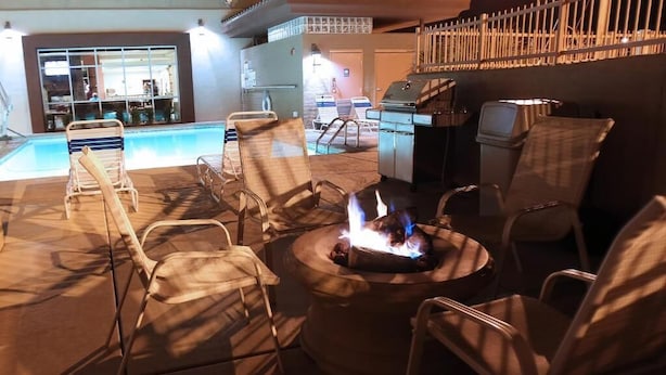 Zona junto a la piscina con sillones de descanso, una chimenea y una zona de bar con una parrilla.