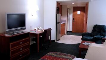Una camera d'albergo con un letto, una scrivania con un computer, una televisione, una sedia, un tavolino e una piccola cucina in secondo piano.