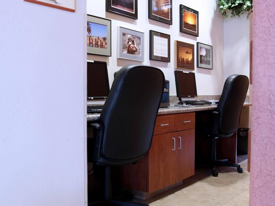 An office with two desks, chairs, a 'BUSINESS CENTER' sign, and framed pictures on the wall.