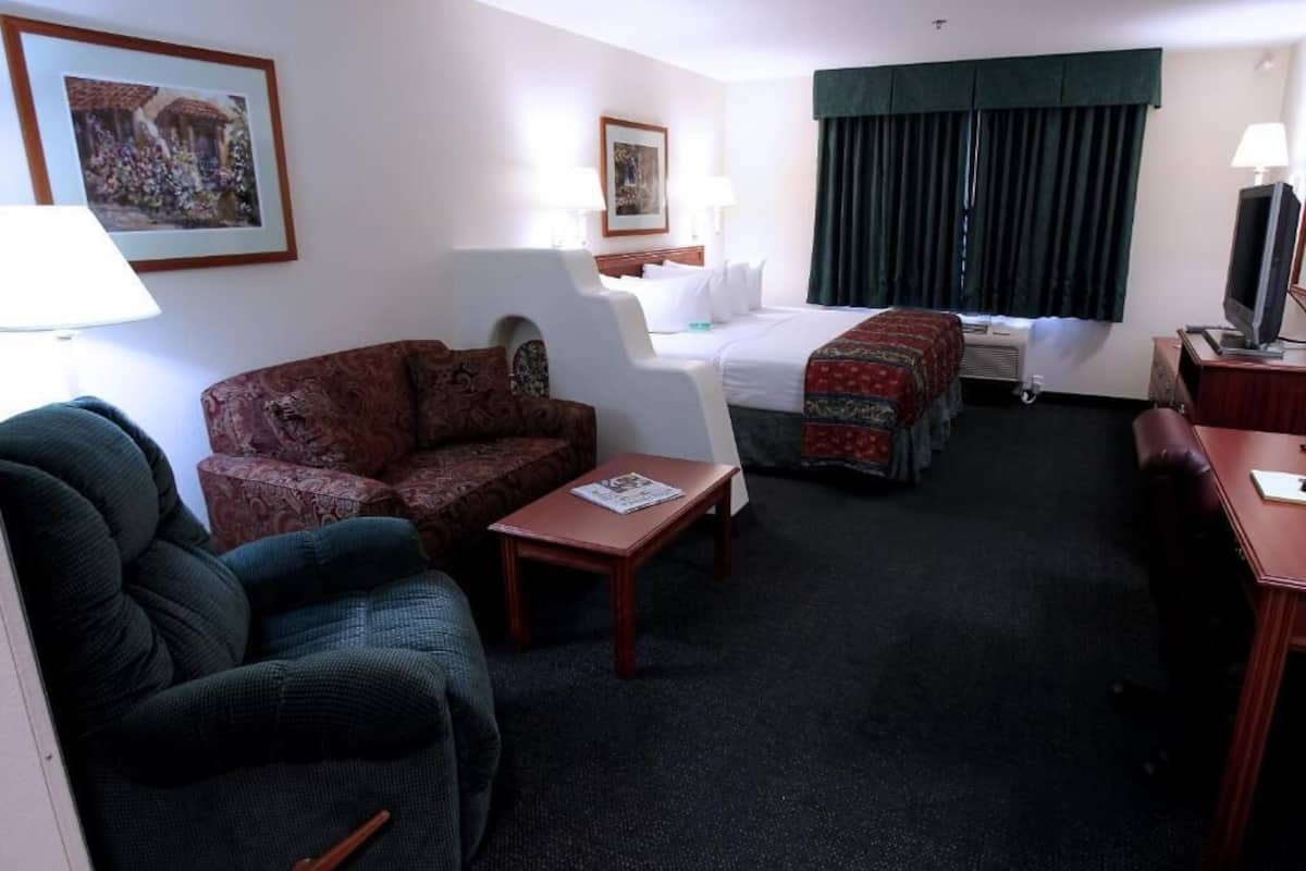 A hotel room with a bed, a sofa, a chair, a small table, and a television.