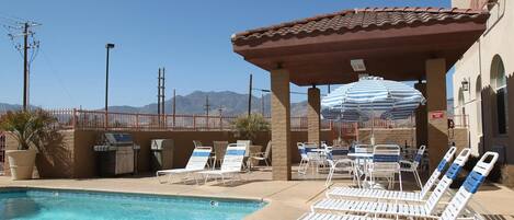 A pool area with lounge chairs, a covered seating area, and a view of mountains in the background.