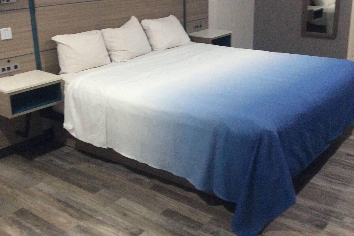 A hotel room with a bed, nightstands, a mirror, and a wooden floor.
