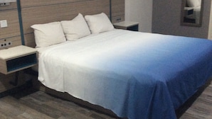 A hotel room with a bed, nightstands, a mirror, and a wooden floor.