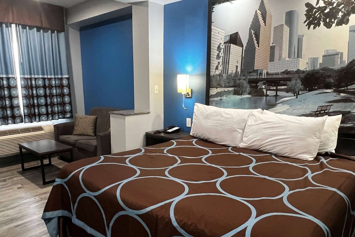 A hotel room with a bed, a sofa, a small table, a nightstand, a lamp, and a window with curtains.