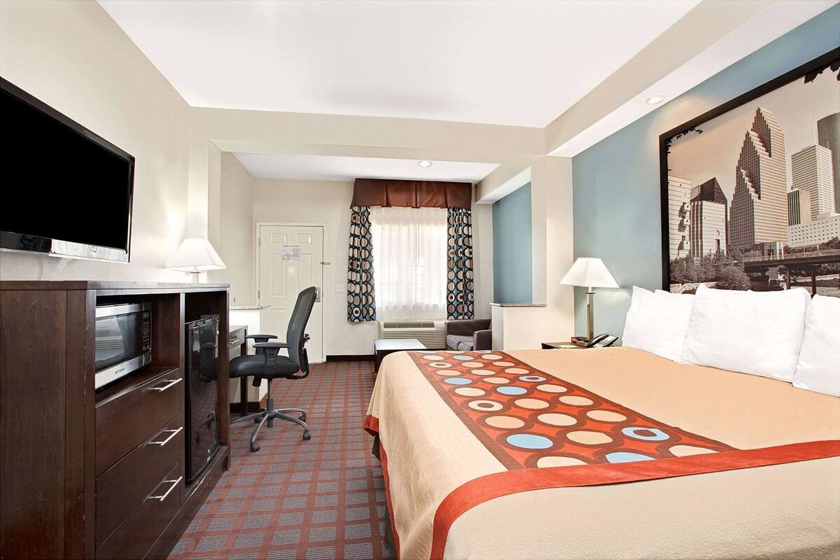 A hotel room with a bed, desk, chair, TV, and a cityscape view.
