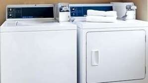 Two stacked front-loading washing machines with control panels, a white towel, and a white container on top. - Crystal Inn Houston North I-45 (Houston)