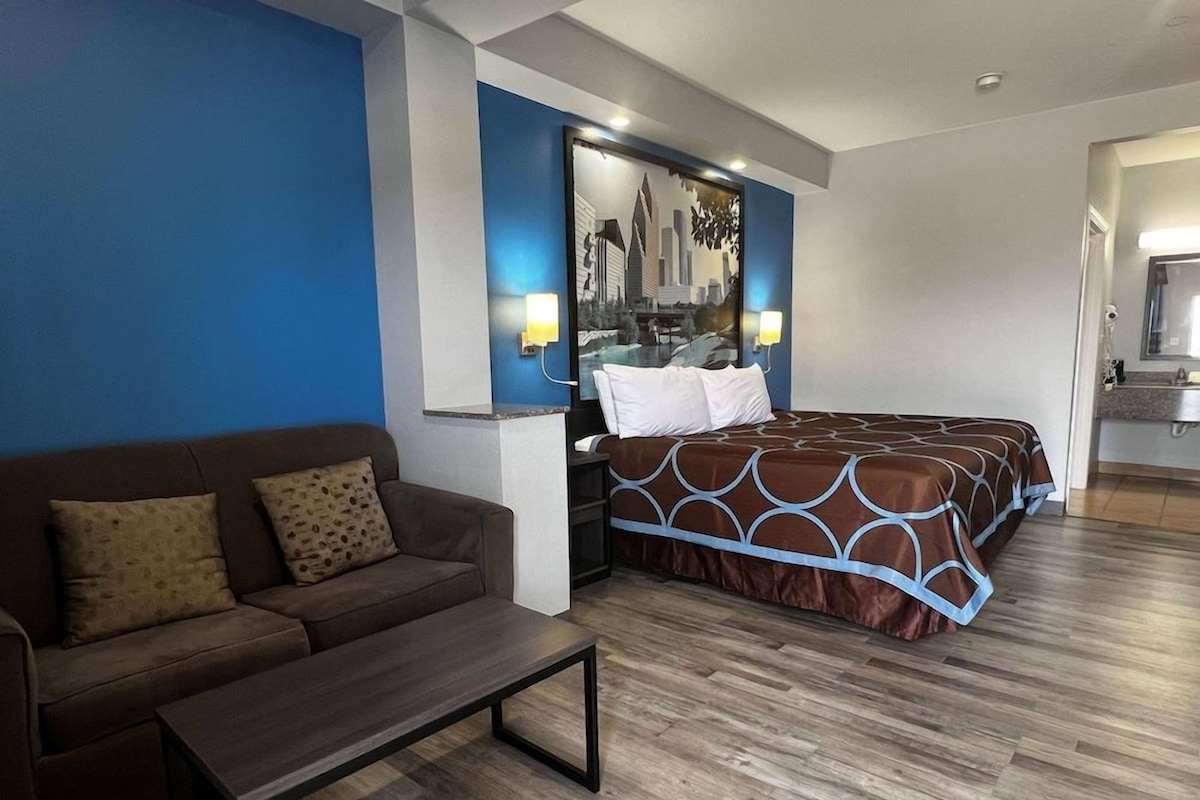 A hotel room with a bed, a sofa, a nightstand, and a mirror.