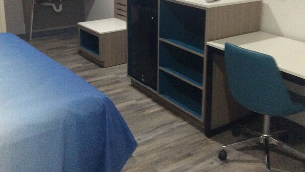 A hotel room with a bed, a desk, a chair, a TV, a wardrobe, and a mirror.