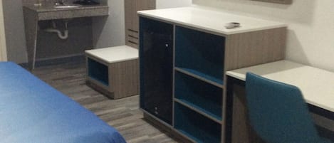 A hotel room with a bed, a desk, a chair, a TV, a wardrobe, and a mirror.