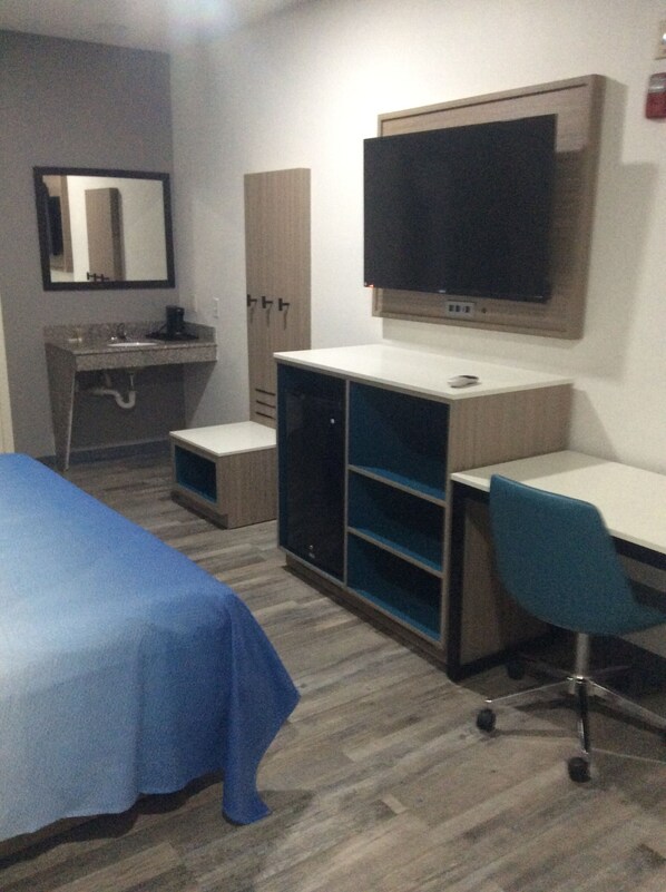 Habitación de hotel con cama, escritorio, silla, televisor, armario y espejo.