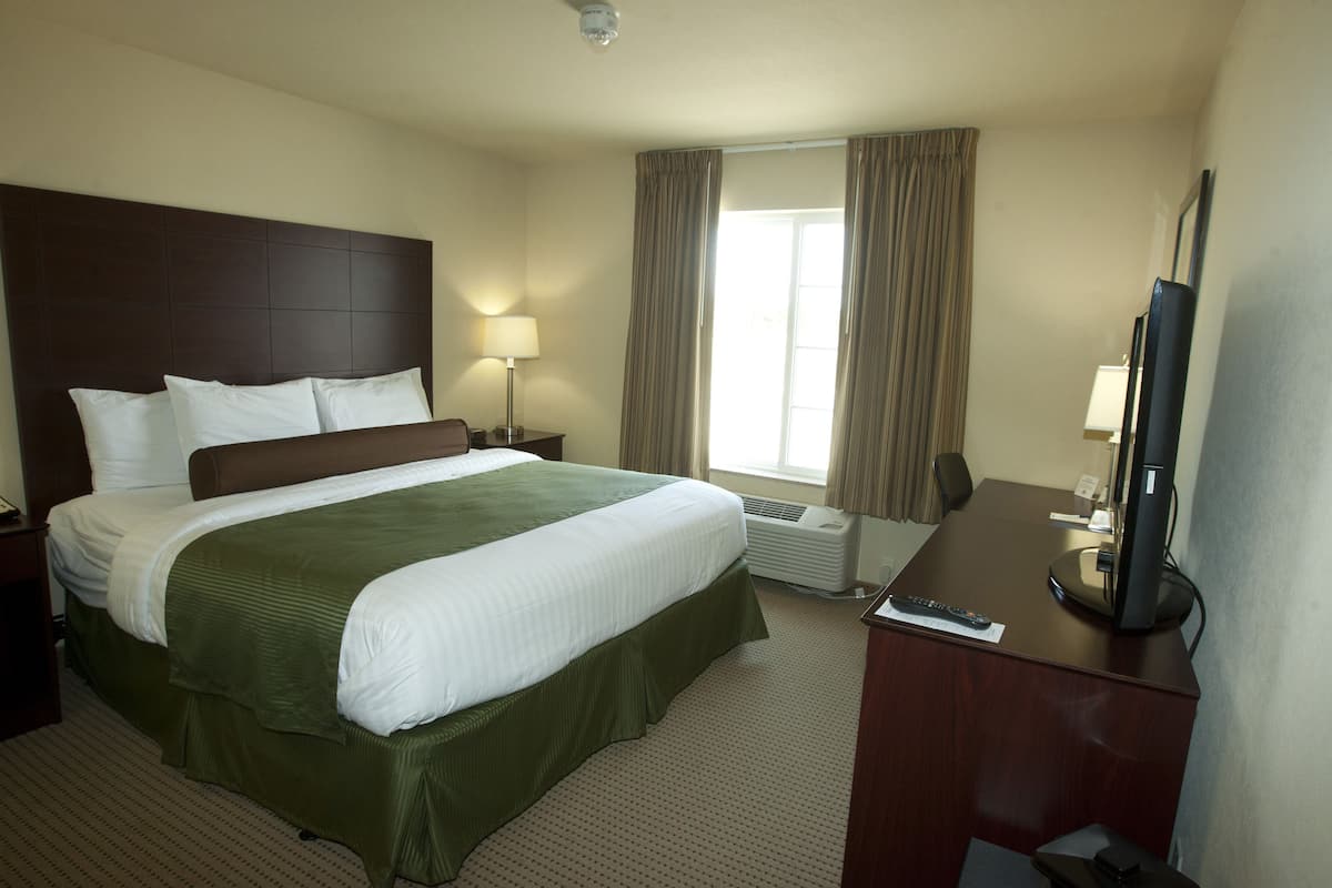 A hotel room with a large bed, a desk with a computer, a TV, and a window with curtains.