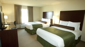 Una habitación de hotel con dos camas, un escritorio con lámpara, televisor y ventana con cortinas.