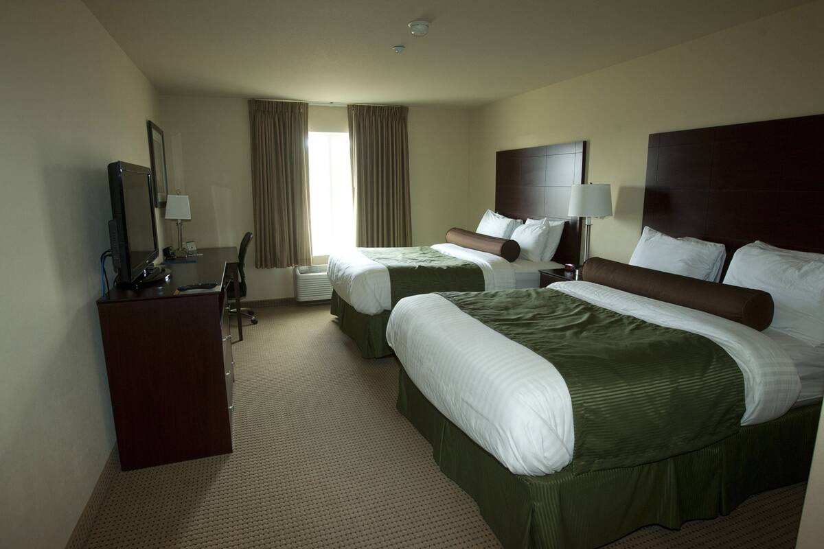A hotel room with two beds, a desk with a computer, and a large window with curtains.