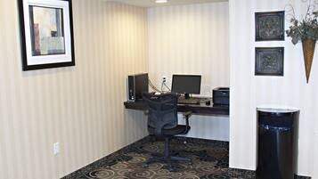 A hotel room with a desk, computer, chair, and a trash can.