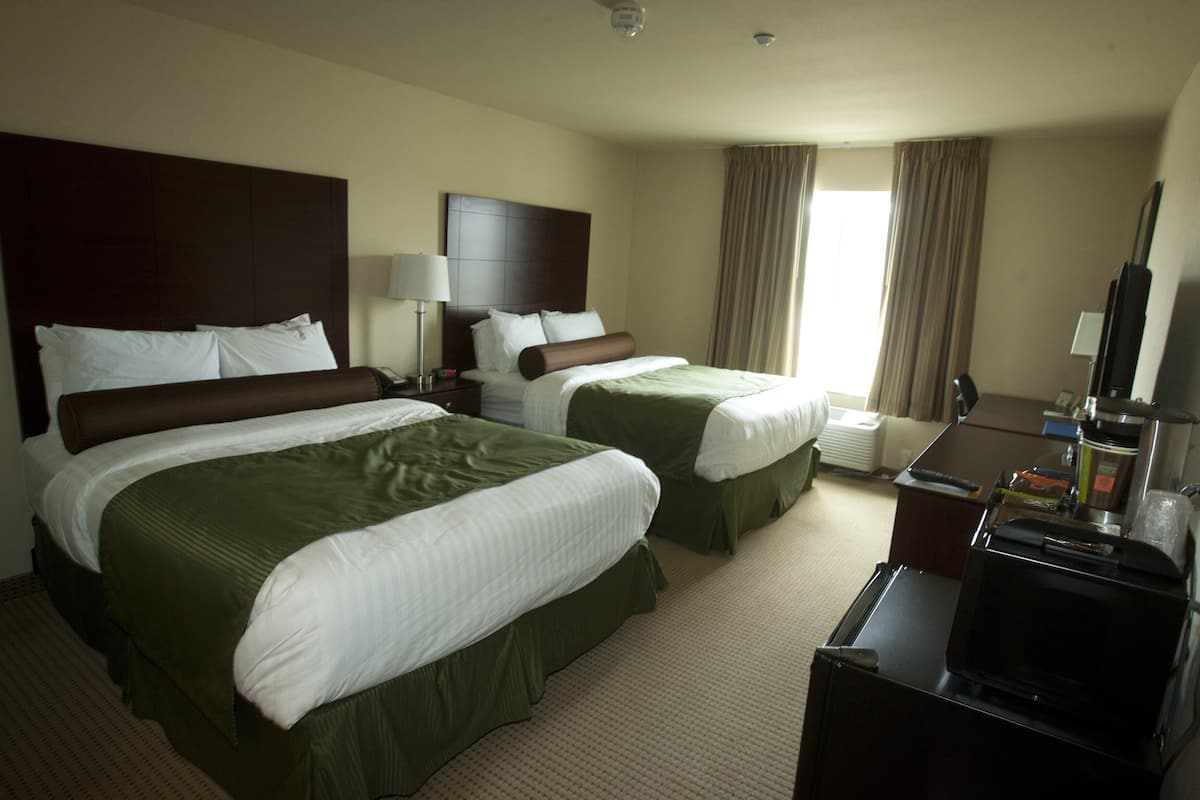 A hotel room with two beds, a desk, a television, and a window with curtains.