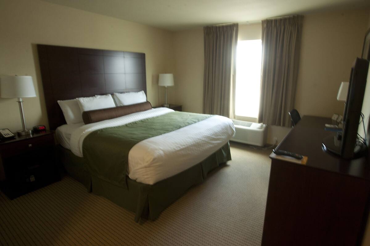 A hotel room with a large bed, two bedside tables with lamps, a desk with a television, and a window with curtains.