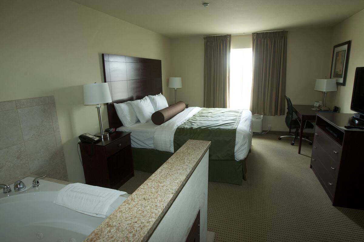A hotel room with a bed, a desk, a chair, a television, a lamp, a telephone, and a bathroom with a bathtub and towel.