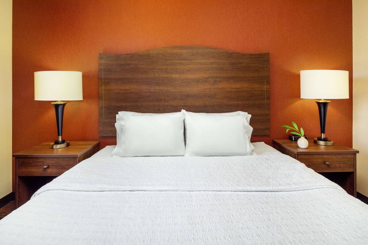 Hotellihuone, jossa on suuri sänky, kaksi yöpöytää valaisimineen ja puinen pääty.